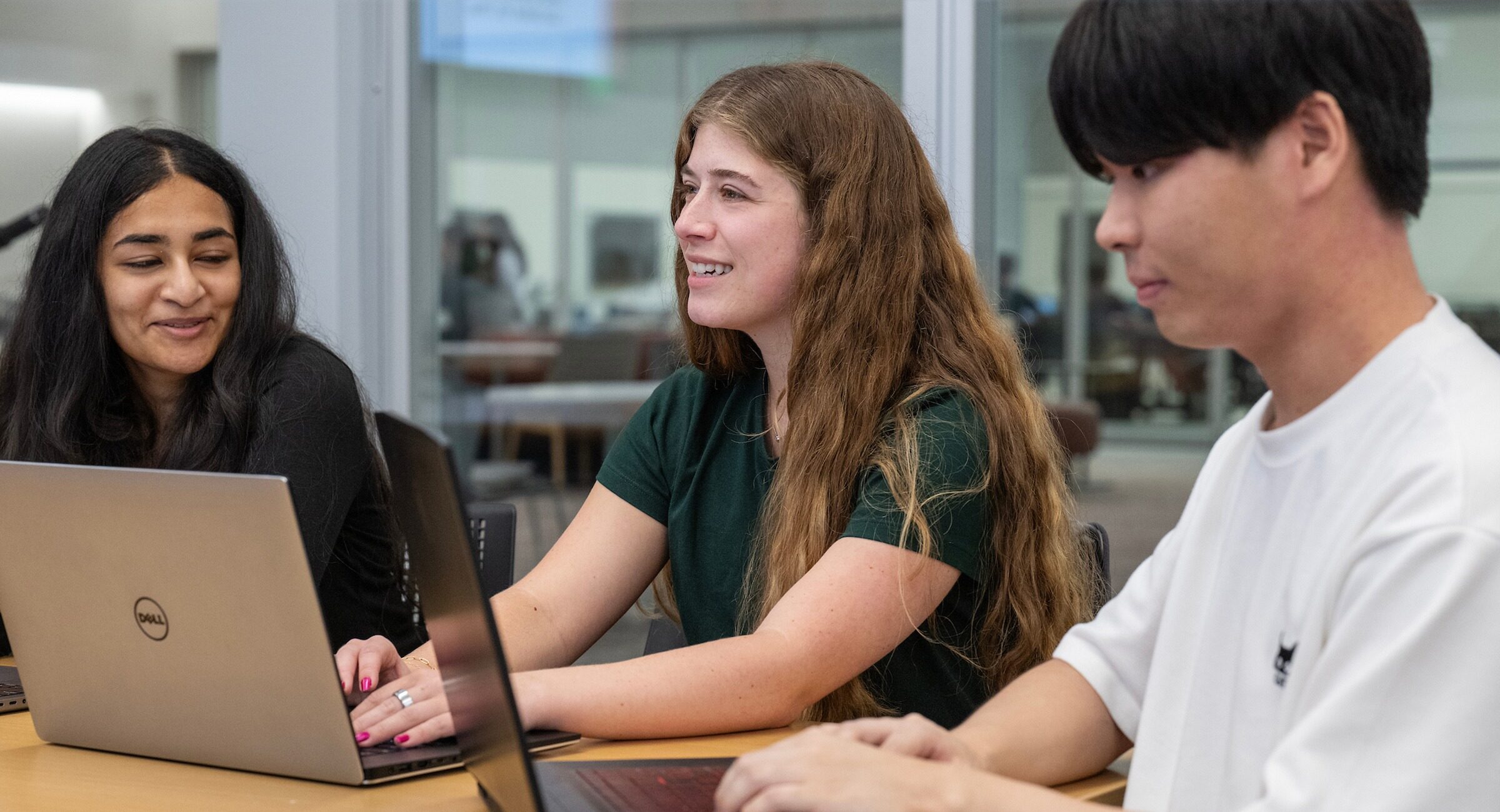 Three students sit at a table and work at their laptops.