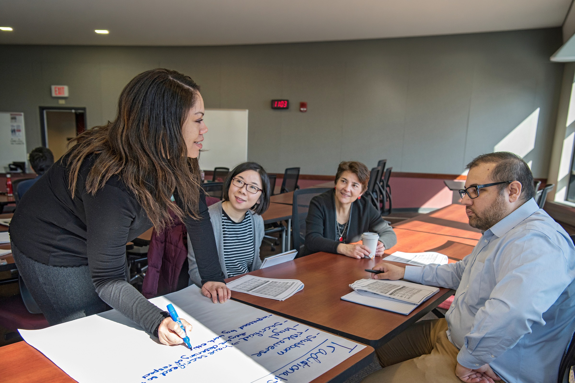 Three students sit at a table with a facilitator while they work together.