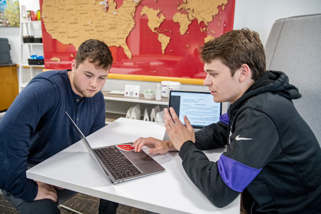 Two students sit and work together on a laptop.