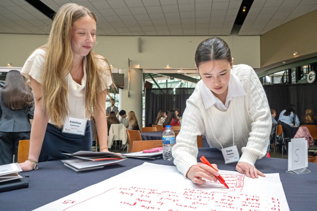 2 students writing in marker on large piece of paper.