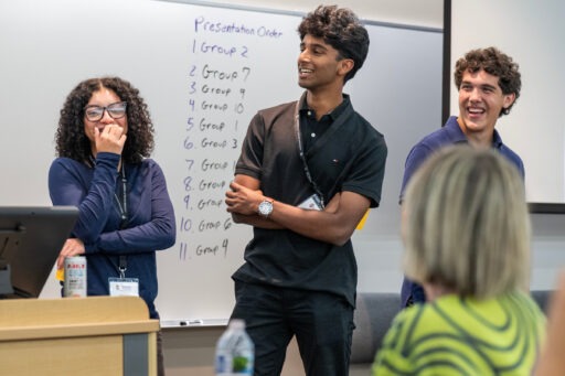 Three students smiling and laughing in front of a dry erase board.