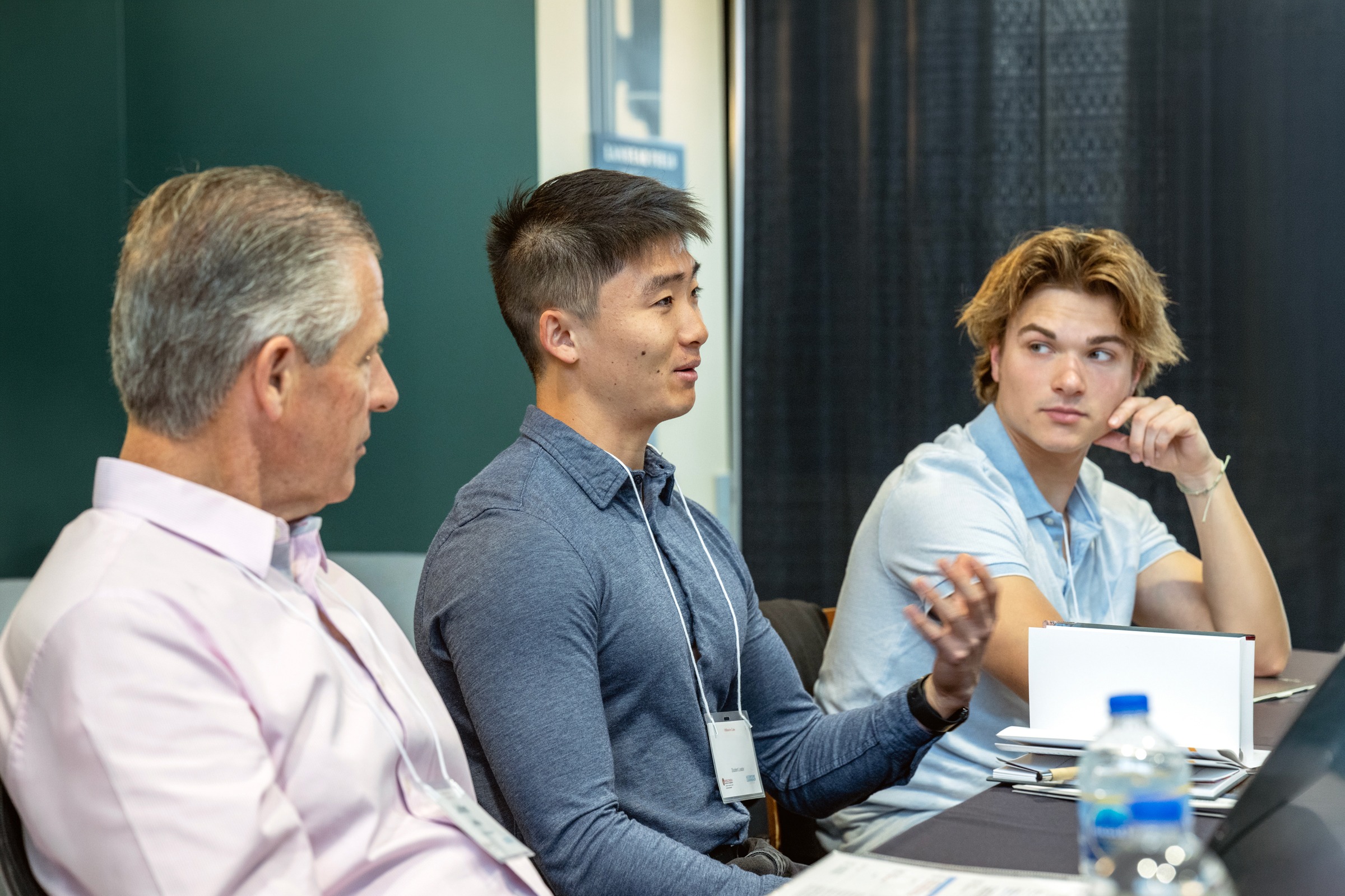 A student talks while seated at a table with another student and a mentor.