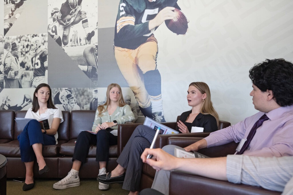 Four students sit in chairs in front of a Green Bay Packers mural.