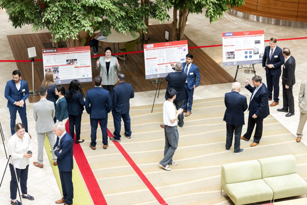 Students walking around during the Executive Advisory Board Meeting and talking with people around Kohl's, Boston Scientific, and Chewy signs.