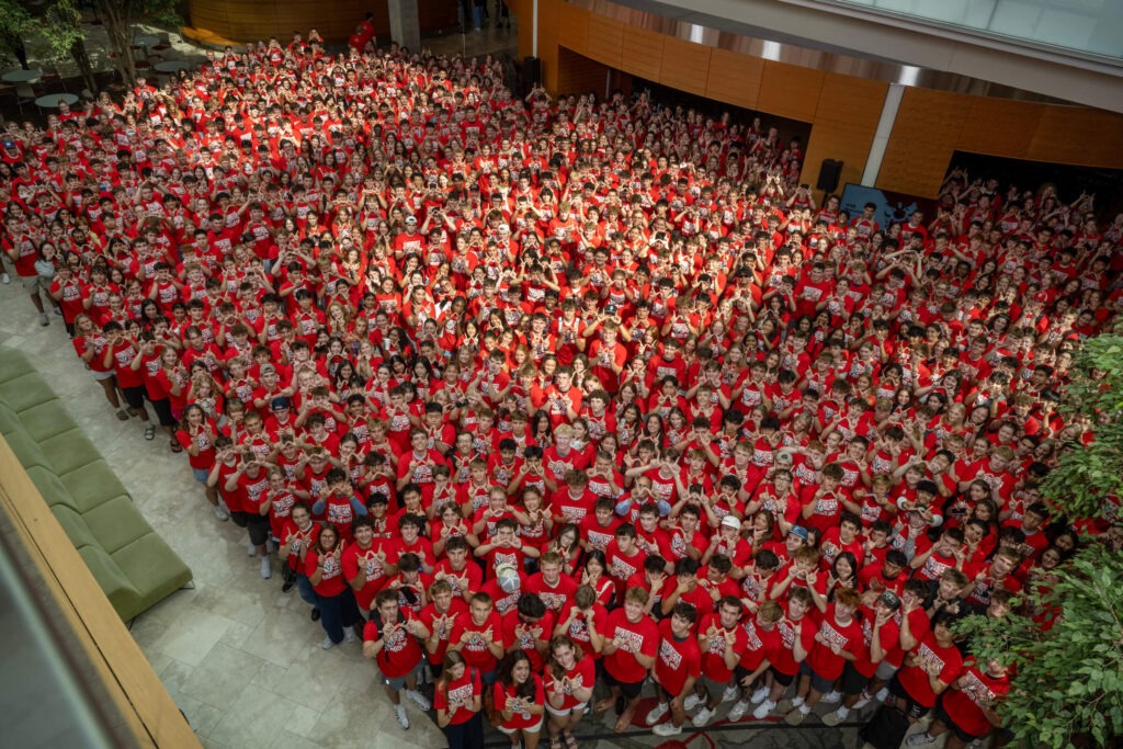 New students wearing red shirts and making a W with their hands.