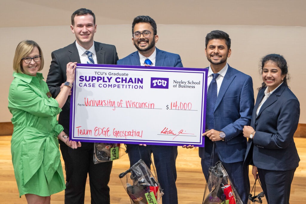 Four students at a supply chain case competition holding a large check with a woman.