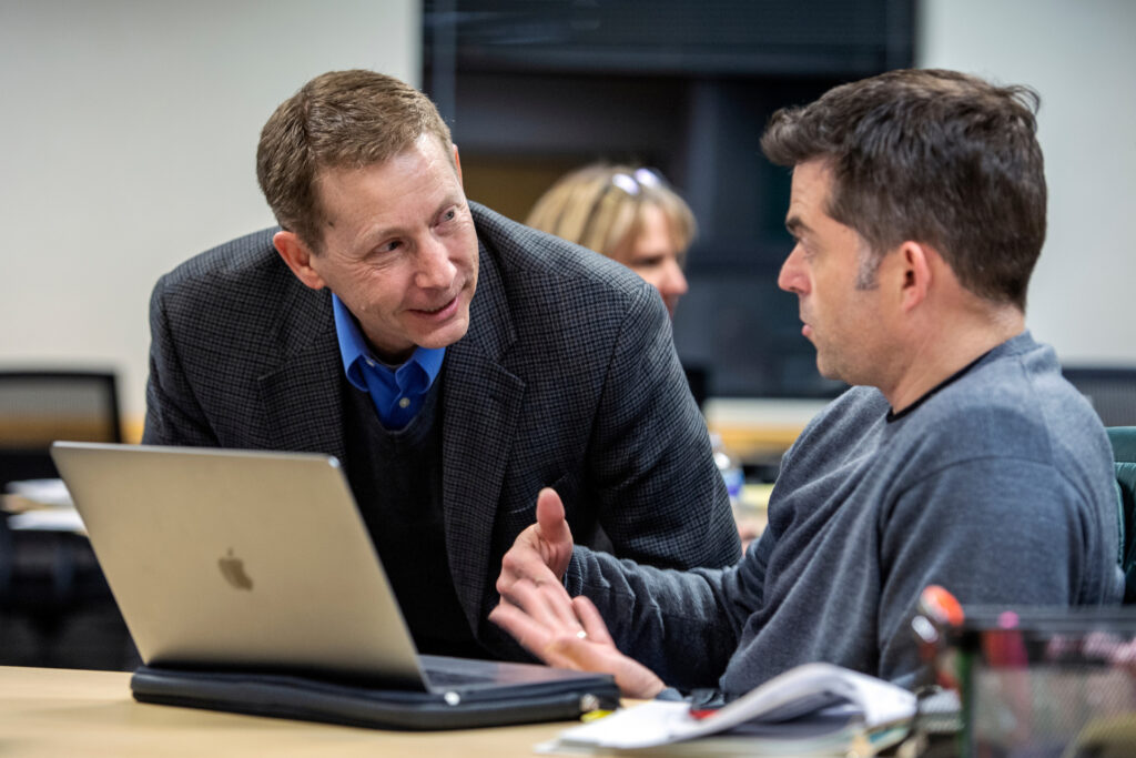 Instructor leaning in to discuss with student in classroom.